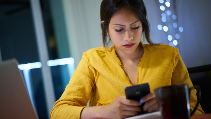 College Student Studying At Night Types Message On Phone